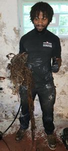 Sewer ninjas worker in a wet suit covered in dirt holding a large mud and trash pile that was causing blockages to a pipe. Cleaned out by the Ninja Drain Cleaning™ system