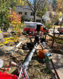 Sewer Ninjas team working on an excavatin repair for sewer system. Company van is parked on the street