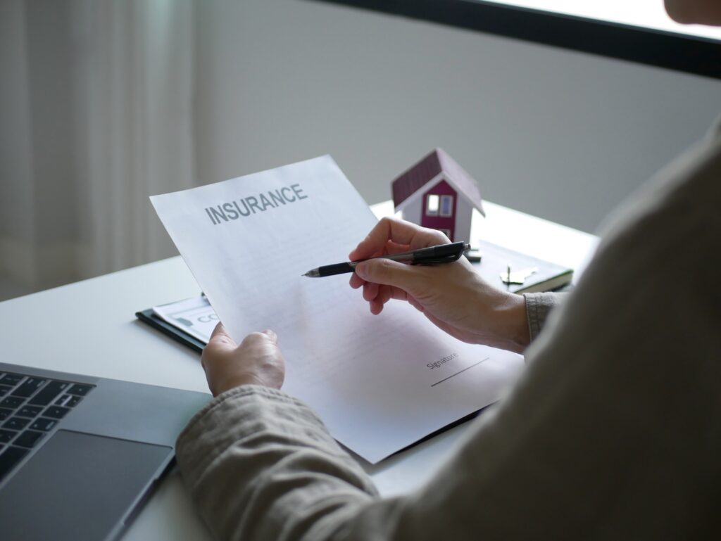 Person looking at a piece of paper that reviews their insurance policy while sitting at a desk. The table has a laptop and a small house decoration